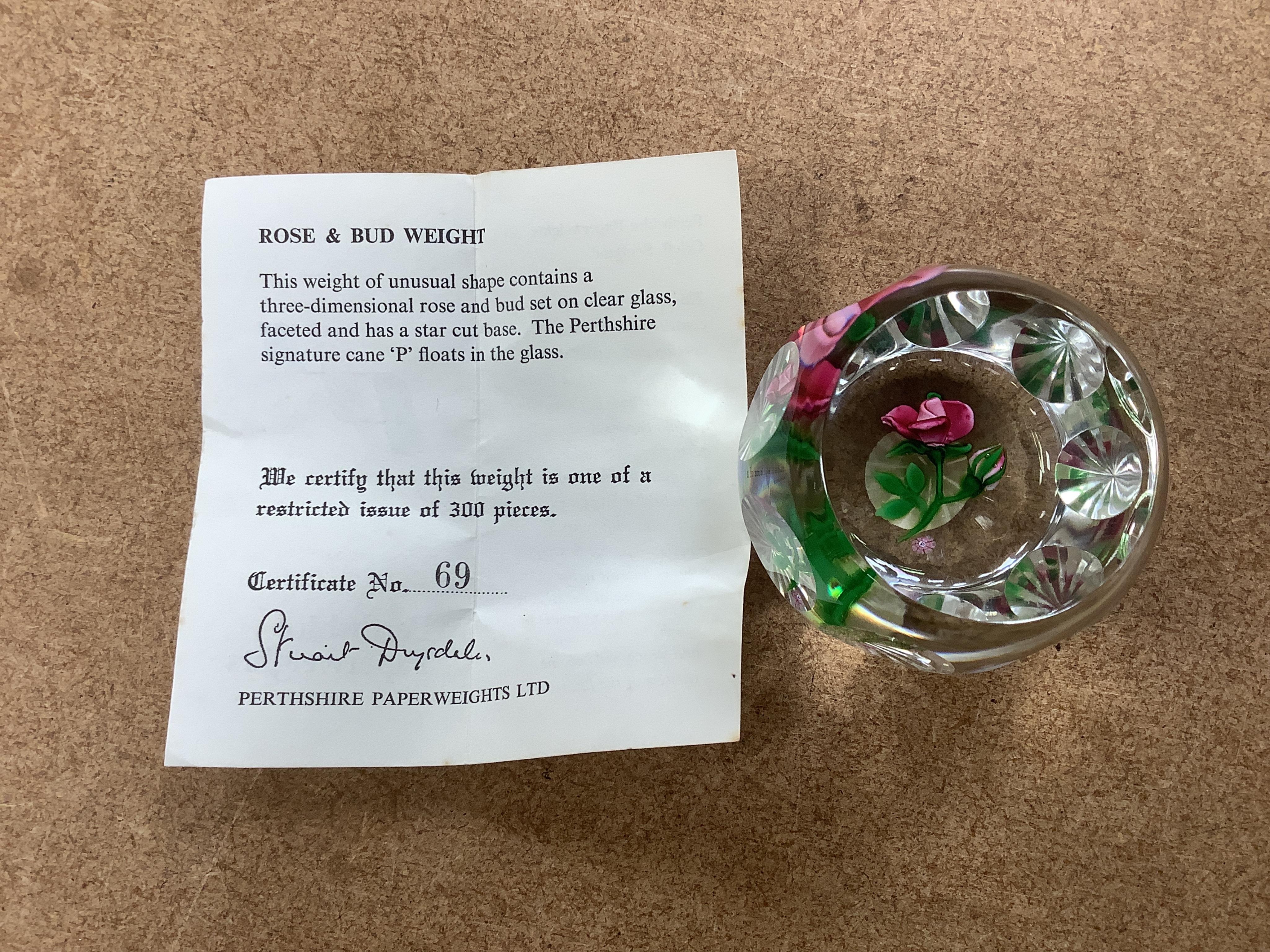 Two Perthshire lamp work glass paperweights, fruit weight, 52/350, rose and bud weight, 69/300 together with a John Deacons bouquet on a ruby base paperweight, edition of 101 (3)
